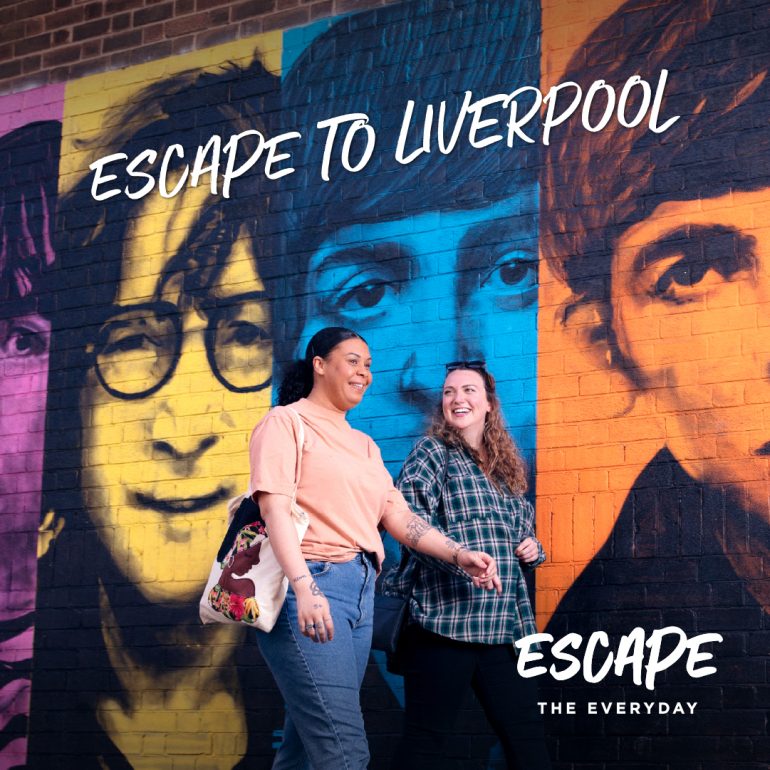 A woman walking in front of a graffiti wall with the logo 'Escape to Liverpool'