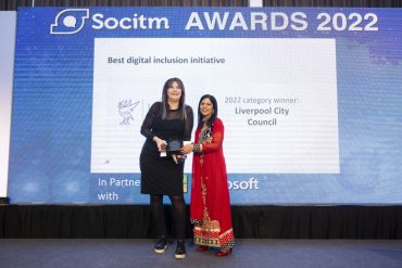 Two women holding an award in front of a screen