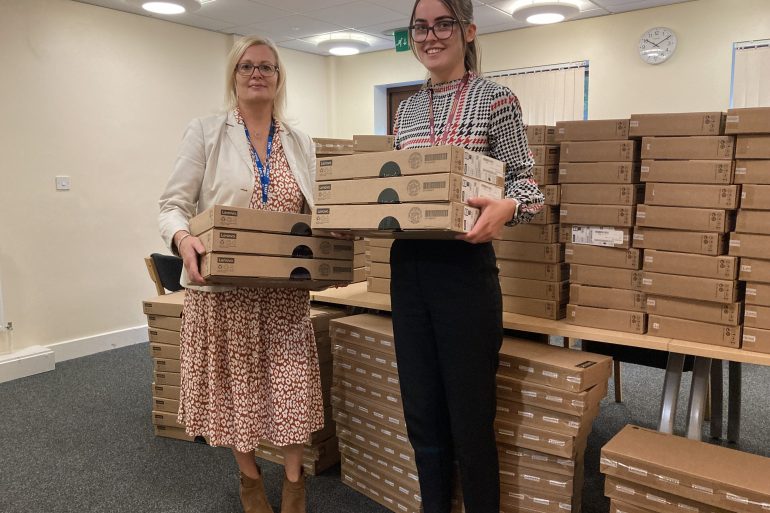 Two women holding boxes in front of a pile of boxes