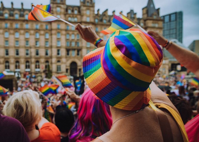 Someone wearing a rainbow hat and waving a Pride flag