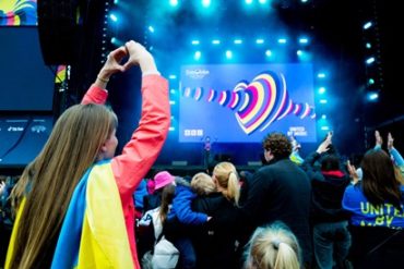 A young girl at the Eurovision village wearing a Ukraine flag and making a love heart shape with her hands