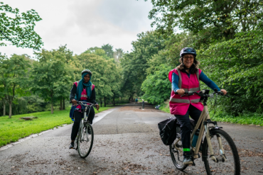 Two women riding on a bike through a park