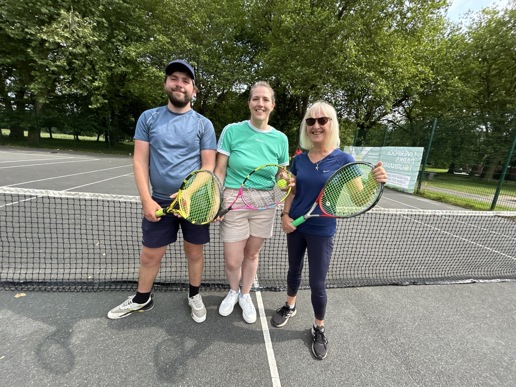 Three people standing on a tennis court holding tennis rackets.