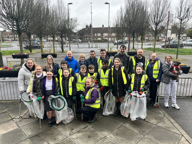 Litter picking volunteers stood in high-vis vests holding bags of litter.