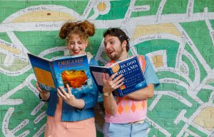 Two people looking at books about dreams standing in front of a map