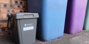A grey food waste caddy next to a blue and purple wheeled bin.