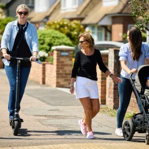 A person riding an e-scooter past two people with a pram