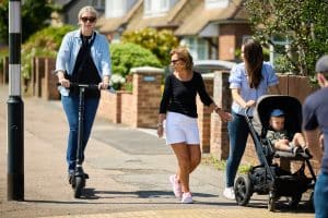 A person riding an e-scooter past two people with a pram