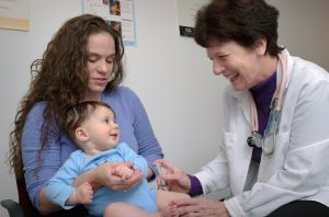 A nurse giving a baby a vaccine. Baby is smiling. Mother is holding the baby.