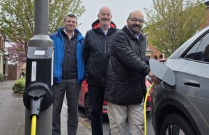 Three people posing behind am electric vehicle charger