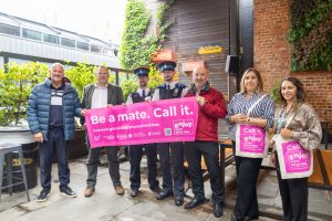 Group of people in bar holding pink sign that reads, call it, be a mate.