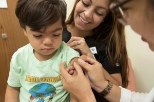 Child getting vaccinated with parent behind smiling