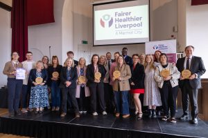 Group of people stood in front on a screen that reads 'Fairer Healthier Liverpool'.
